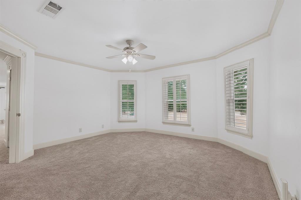 Neutral-toned carpeted flooring, multiple windows with plantation shutters, crown molding, and a ceiling fan with integrated lighting