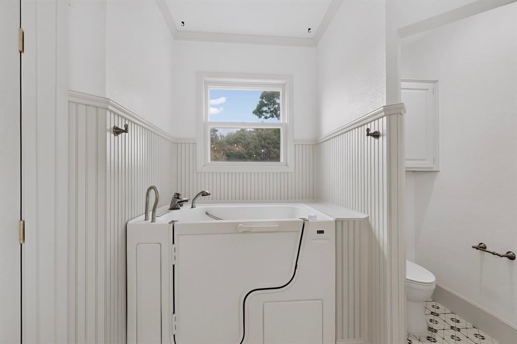 Walk-in bathtub with chrome fixtures, wainscoting, window with exterior scenery, and patterned tile flooring