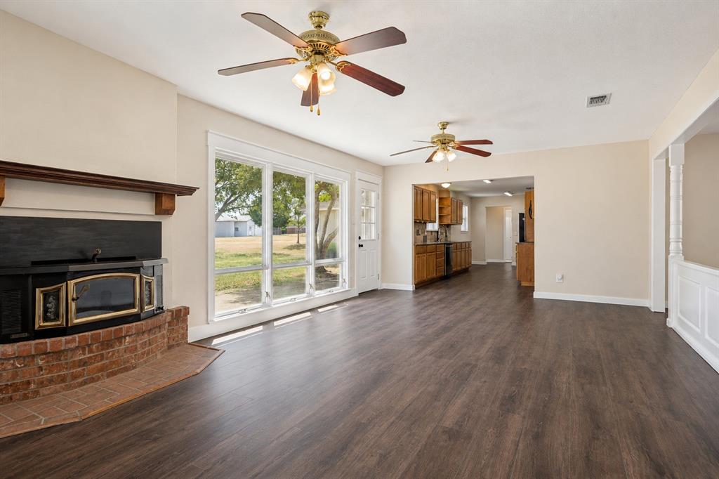 Wood-finish flooring, brick-surround fireplace with wood mantel, multiple ceiling fans, and a multi-pane glass door leading to an exterior