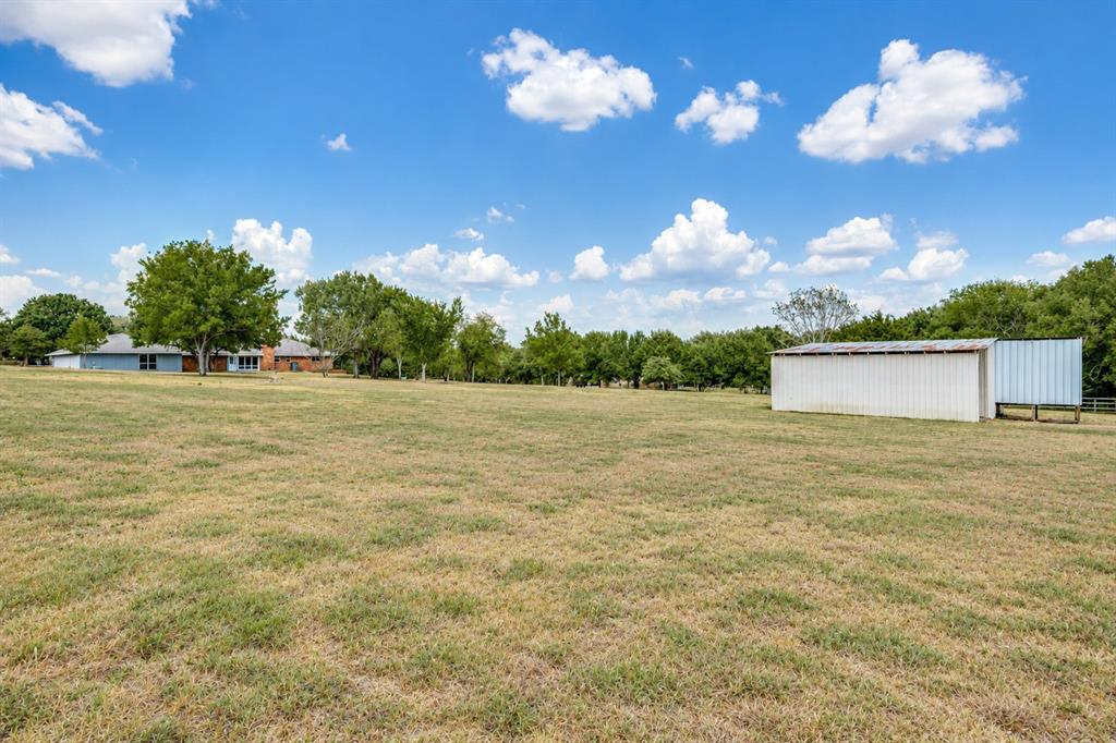 Expansive grassy area featuring a white metal outbuilding and mature trees