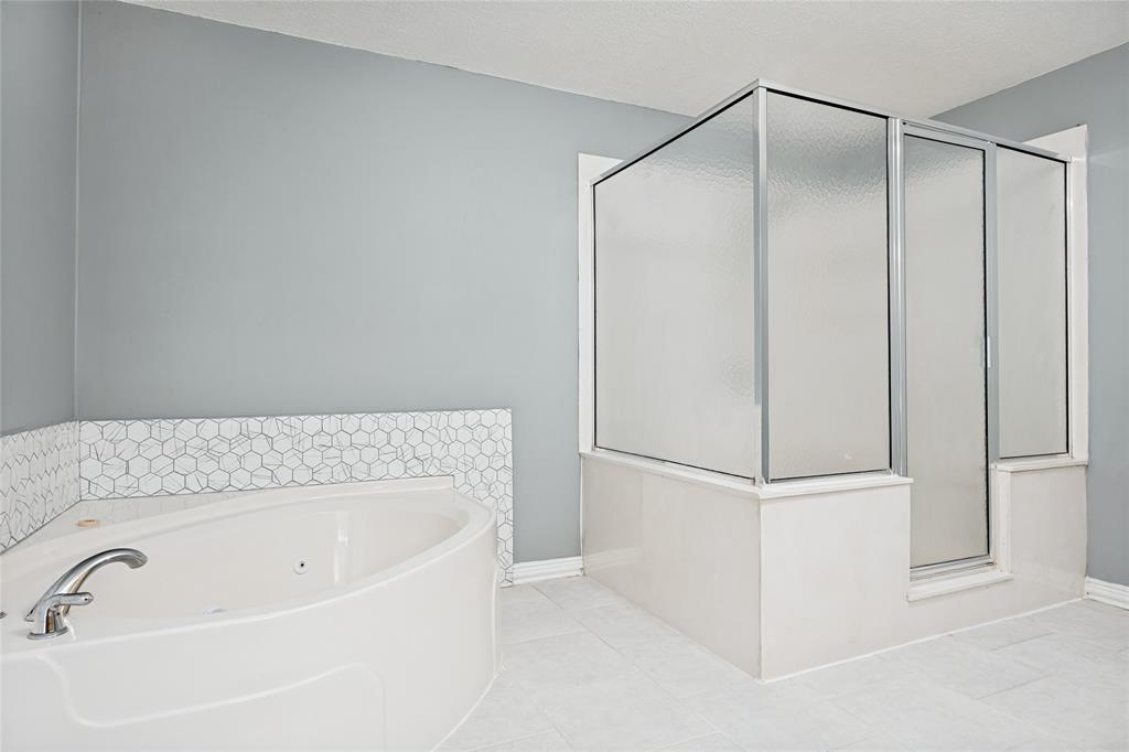 Corner tub, glass-enclosed shower, polished chrome fixtures, hexagonal tile accent, and light-toned floor tile