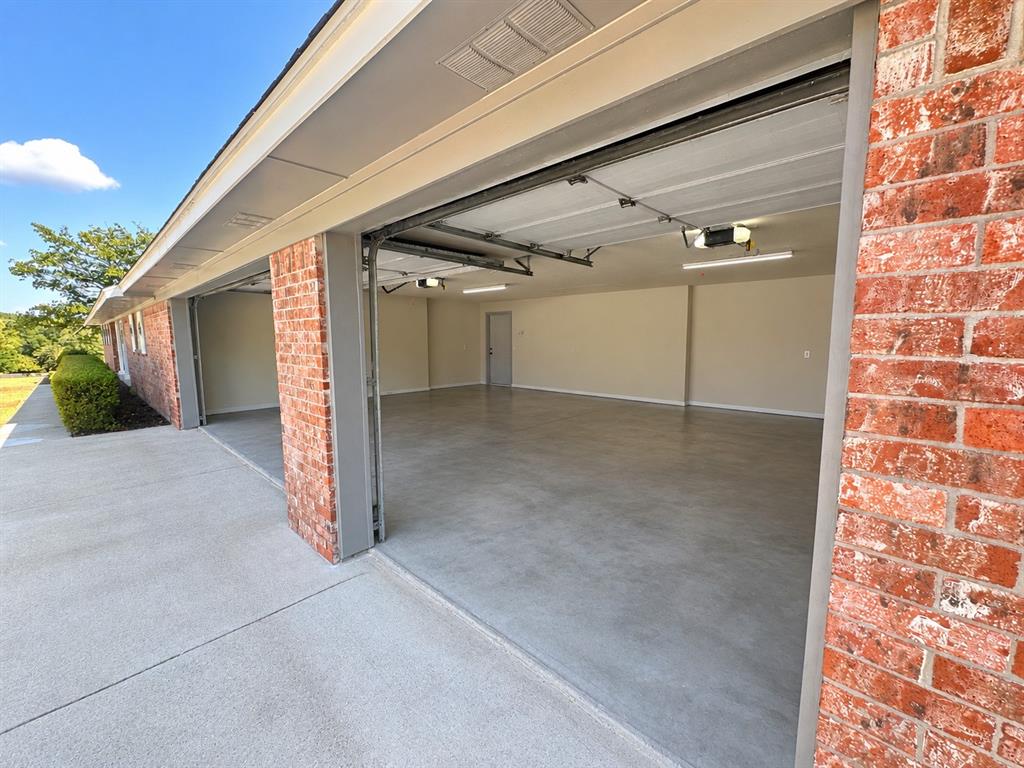 Spacious multi-car garage with brick exterior, concrete flooring, and overhead lighting