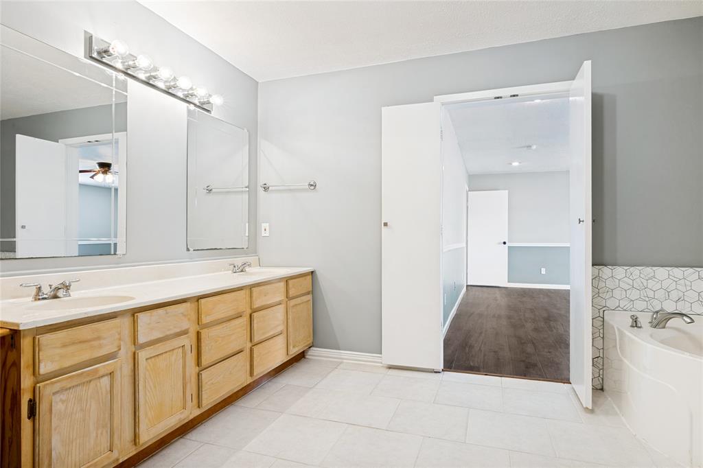 Double vanity with integrated sinks, large mirrors, overhead lighting fixture, hexagonal tile accent, and a built-in tub