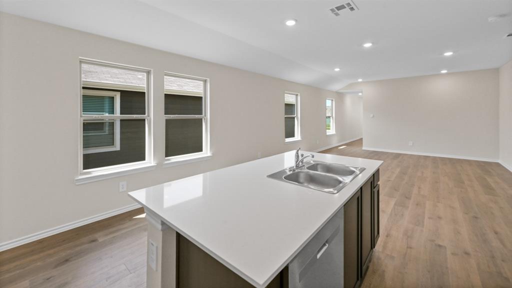 Kitchen island featuring a double basin stainless steel sink with a single-handle pull-down faucet, a white countertop, and dark wood-finish cabinetry