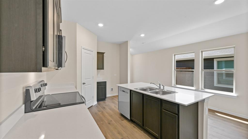 Kitchen featuring an island with double basin sink, quartz countertops, wood-finish flooring, dark wood cabinetry, and recessed lighting