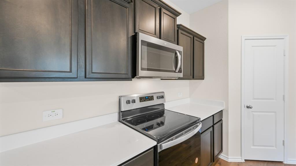Kitchen featuring dark wood-finish cabinetry, white solid surface countertops, a stainless steel range, and an over-the-range microwave