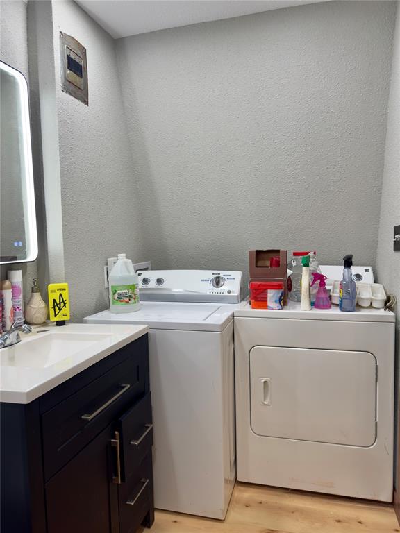 Laundry area featuring separate washer and dryer, a textured wall, a sink, and light wood-type flooring