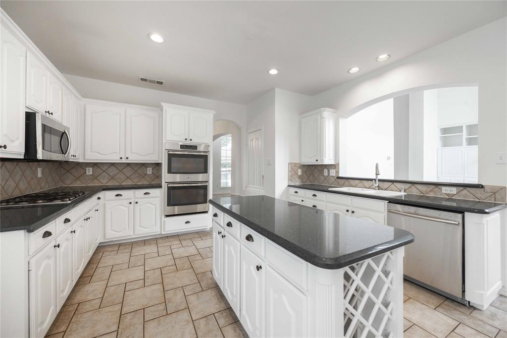 White cabinetry with black hardware, dark countertops, a stainless steel double oven, and tiled flooring White cabinetry with black hardware, dark countertops, a stainless steel double oven, and tiled flooring