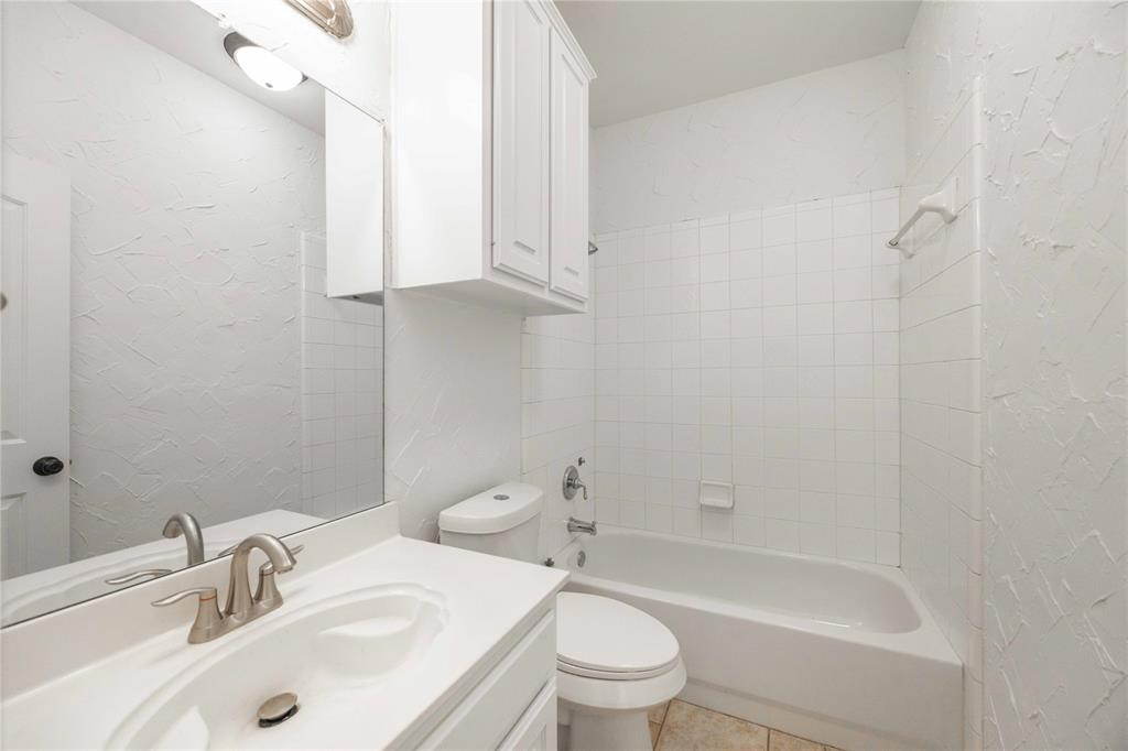White vanity with integrated sink, brushed nickel faucet, wall-mounted mirror, white shaker-style cabinetry, and a full bathtub with white subway tile surround