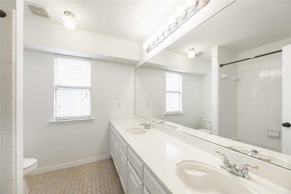 Dual vanity with integrated sinks, expansive mirror, a window with blinds, and white tile tub/shower combination
