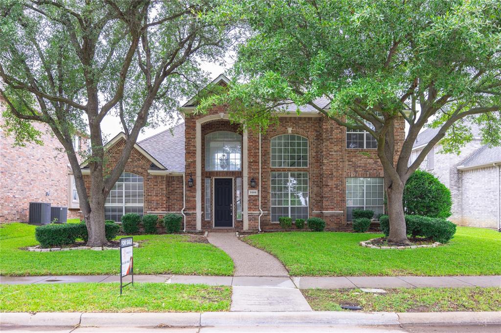 Brick facade residence featuring mature trees, a manicured lawn, an arched window, and a prominent front entry