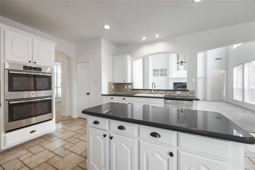 Kitchen featuring white cabinetry, stainless steel double ovens, a center island with a dark countertop, and tiled flooring