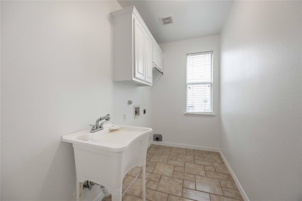 Utility sink, upper cabinetry, window with blinds, and tile flooring