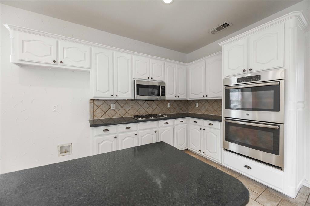 White cabinetry, double wall ovens, stainless steel microwave, and dark countertops