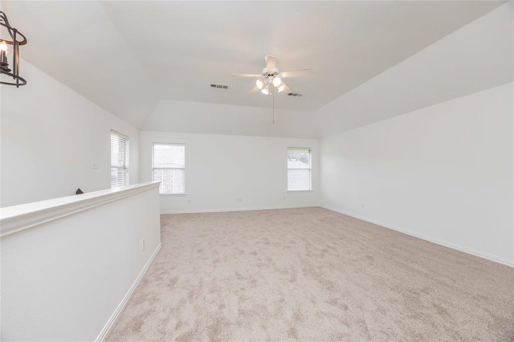 Spacious room featuring vaulted ceilings, neutral carpeting, two windows, and a ceiling fan