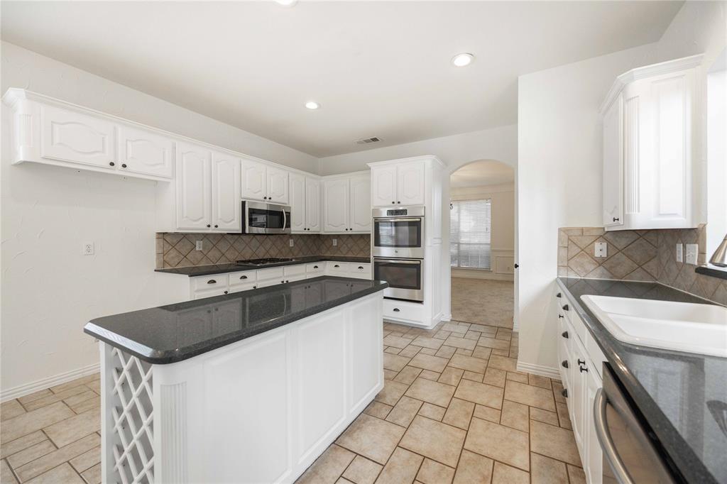 White cabinetry with dark hardware, stone-finish countertops, stainless steel appliances, tiled backsplash, and tiled flooring White cabinetry with dark hardware, stone-finish countertops, stainless steel appliances, tiled backsplash, and tiled flooring