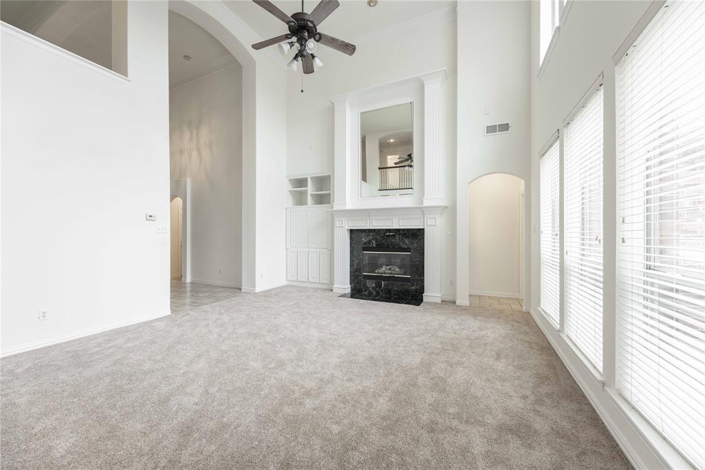Spacious living area featuring high ceilings, a fireplace with a dark stone surround, tall windows with blinds, a ceiling fan, and light-toned carpeting