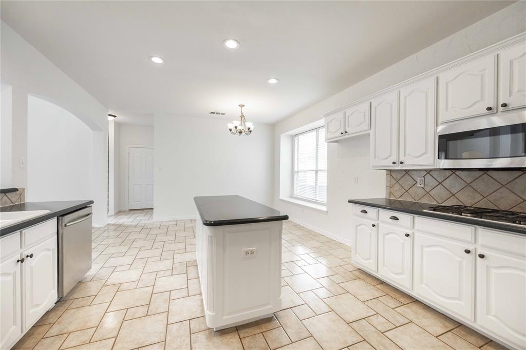 Kitchen featuring white cabinetry, dark countertops, a tile backsplash, stainless steel appliances, and a central island Kitchen featuring white cabinetry, dark countertops, a tile backsplash, stainless steel appliances, and a central island