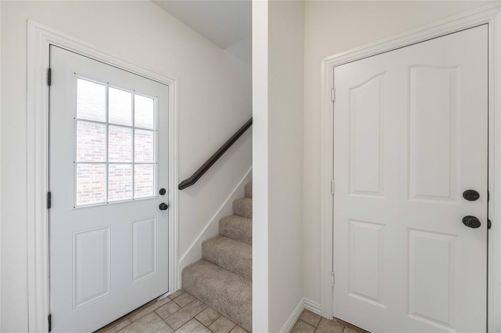 Entryway featuring a paneled door with nine-lite glass, neutral tile flooring, and carpeted stairs with a dark wood handrail