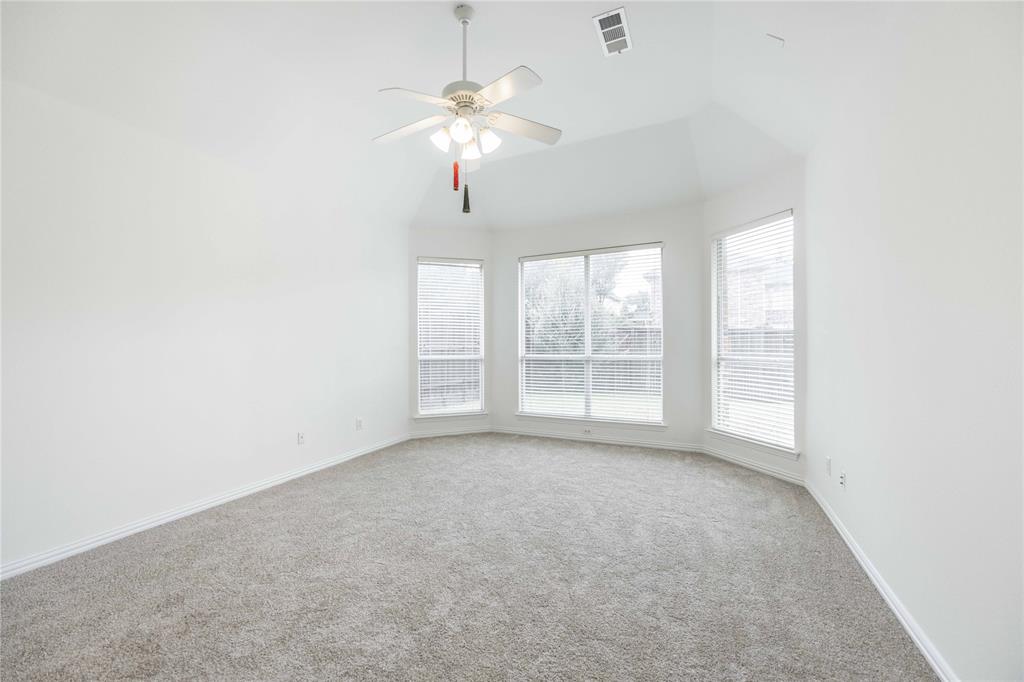 Vaulted ceiling with a ceiling fan, bay window configuration, multiple windows with blinds, and light-toned carpeting