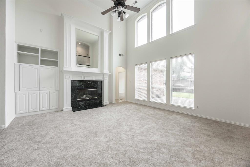 Two-story living area with high ceilings, a built-in media cabinet, a fireplace with a dark stone surround, and multiple windows