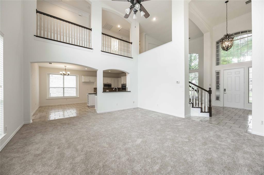 Two-story ceiling, arched doorways, white interior paint, wood-finish staircase with white balusters, and a decorative chandelier