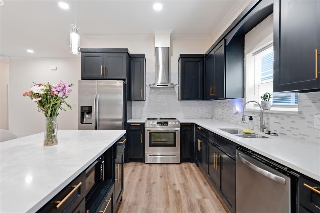 Kitchen featuring dark cabinetry with gold-tone hardware, stainless steel appliances, light countertops, a white tile backsplash, and Luxury Vinyl Flooring
