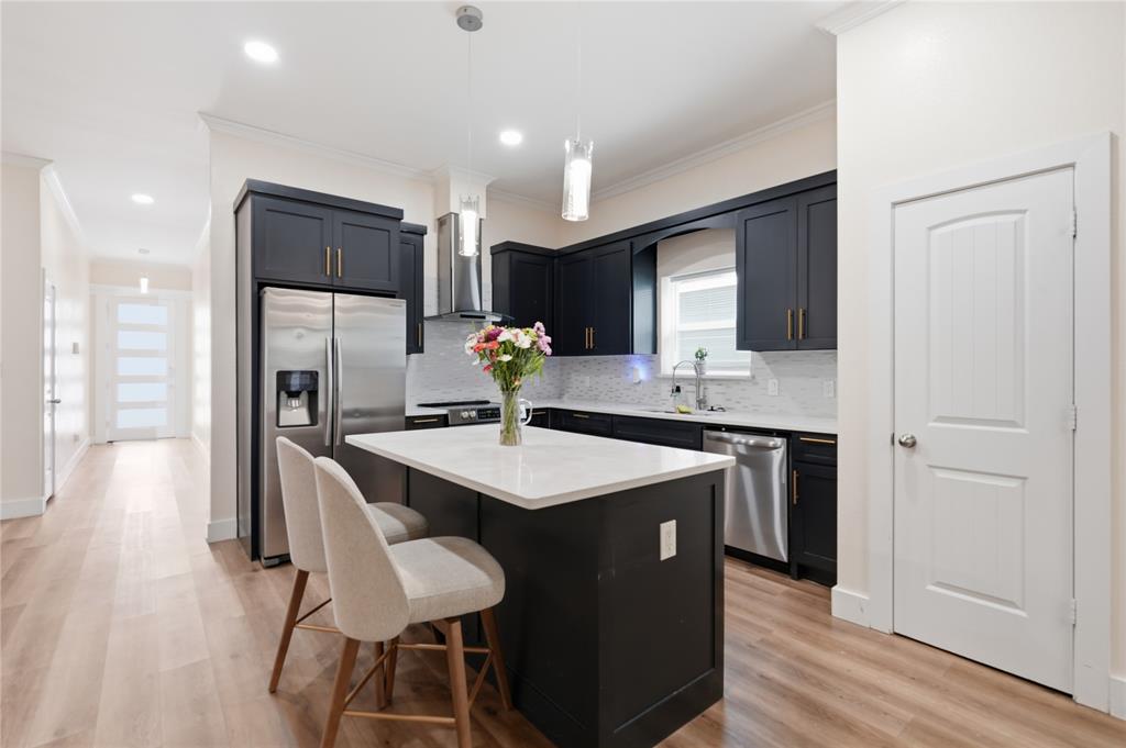 Modern kitchen featuring dark cabinetry with gold-tone hardware, stainless steel appliances, a white tile backsplash, and a central island with a white countertop