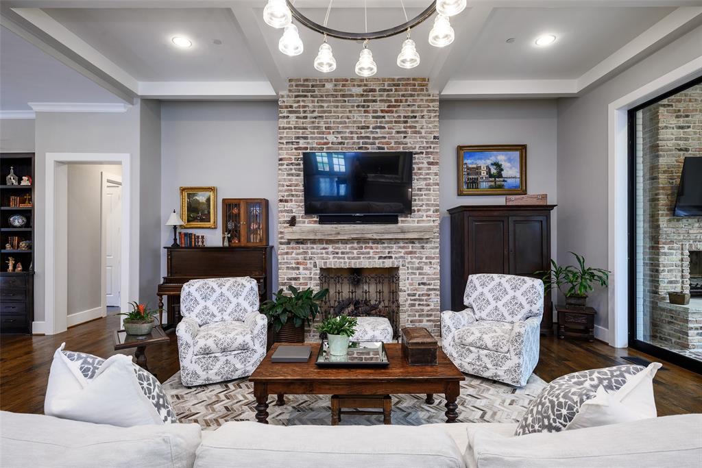 Exposed brick fireplace with a wood-mantel, tray ceiling, recessed lighting, and wood-finish flooring