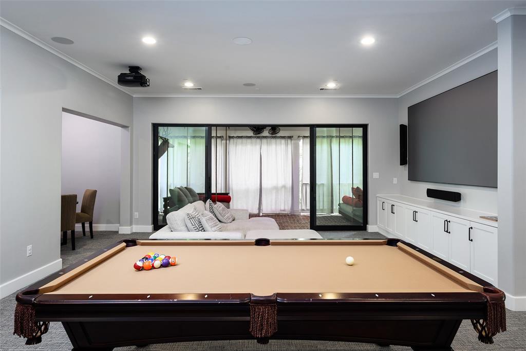 Recessed lighting, built-in cabinetry with dark hardware, large wall-mounted screen, and sliding glass doors