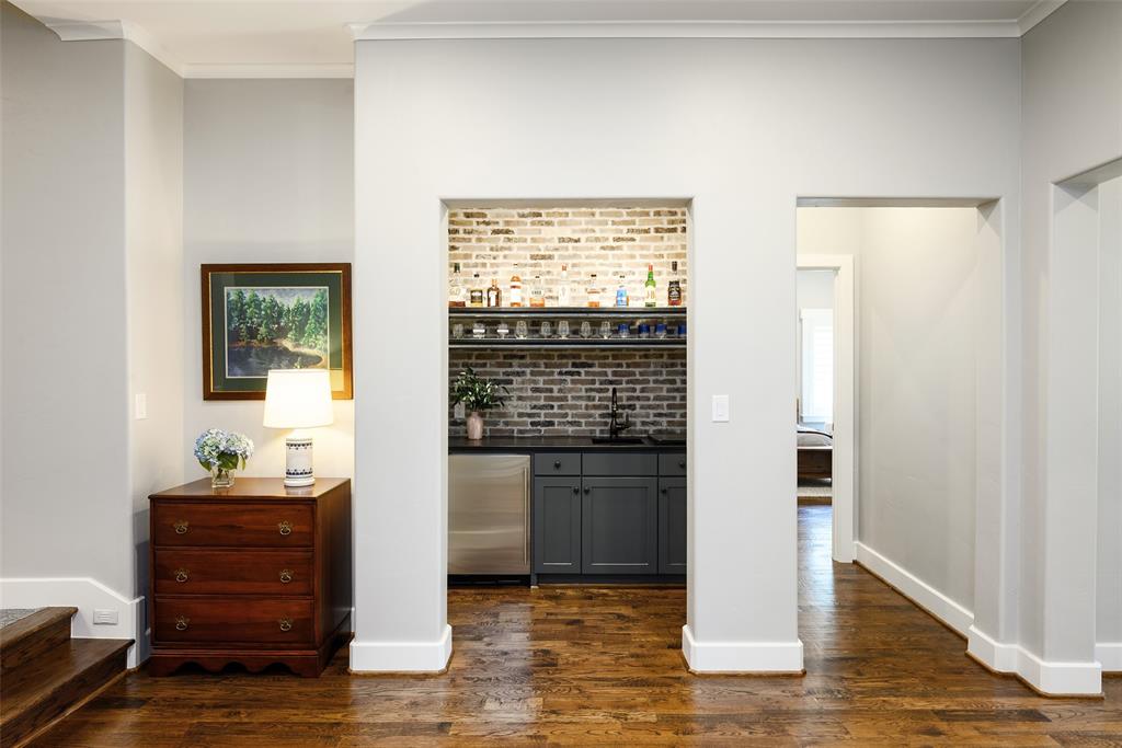 Built-in wet bar featuring a brick accent wall, stainless steel beverage refrigerator, dark cabinetry, and a dark countertop