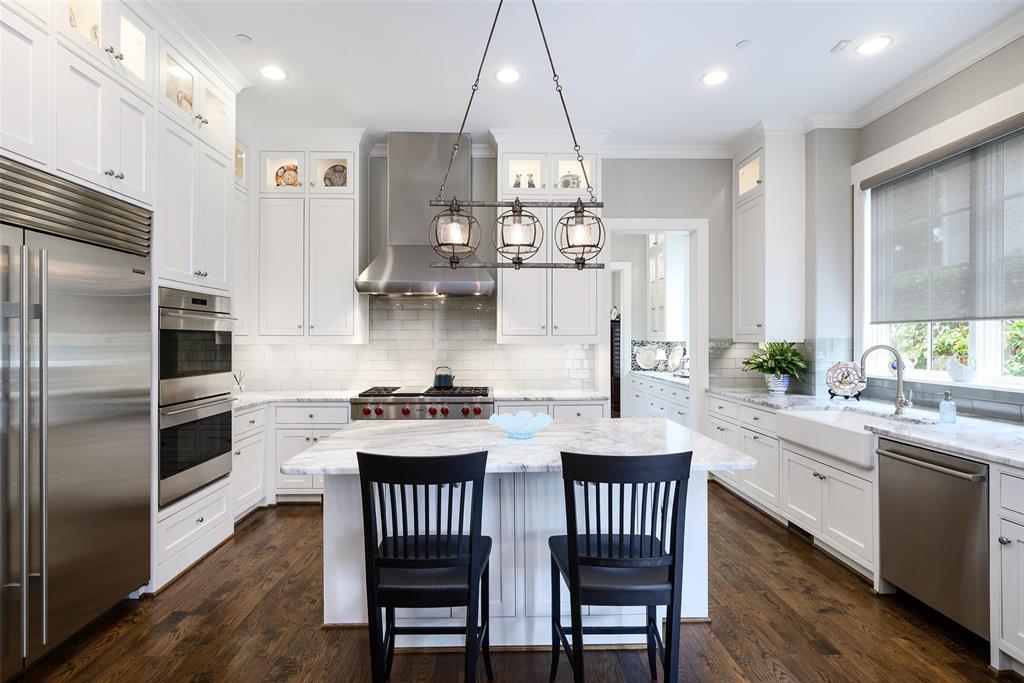 Gourmet kitchen featuring white cabinetry, stainless steel appliances, a center island with countertop seating, a farmhouse sink, and wood-finish flooring