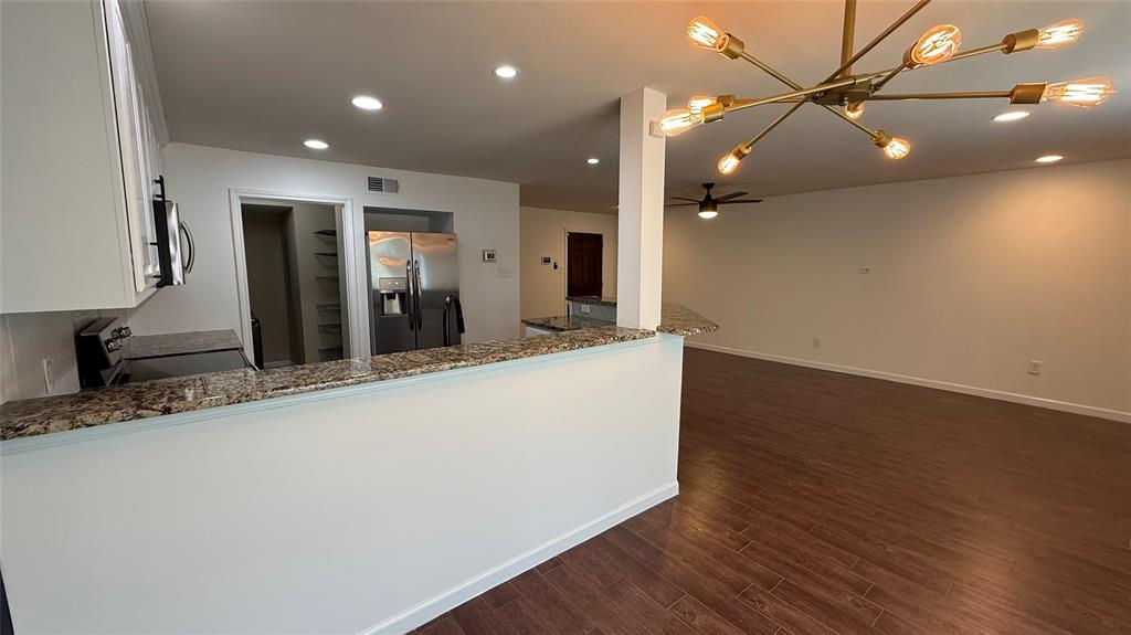 Wood-finish flooring, recessed lighting, and a contemporary chandelier illuminate the open living space