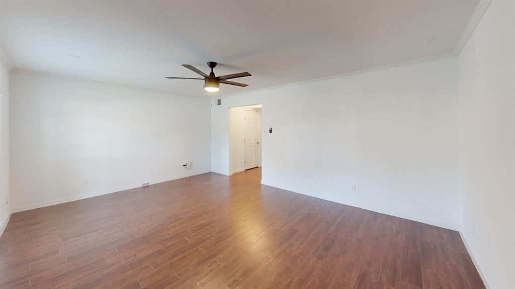 Spacious interior featuring wood-finish flooring, white walls, and a ceiling fan with integrated lighting