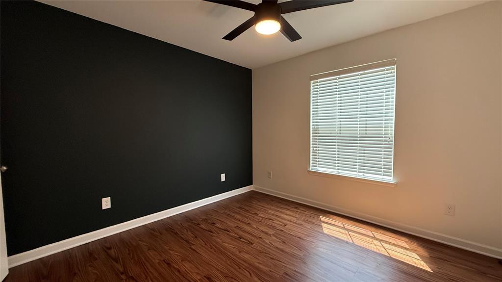 Wood-finish flooring, accent wall, ceiling fan with integrated lighting, and window with blinds