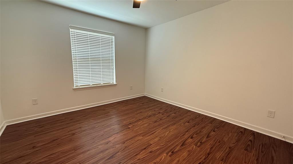 Spacious room featuring wood-finish flooring, a window with blinds, and a ceiling fan