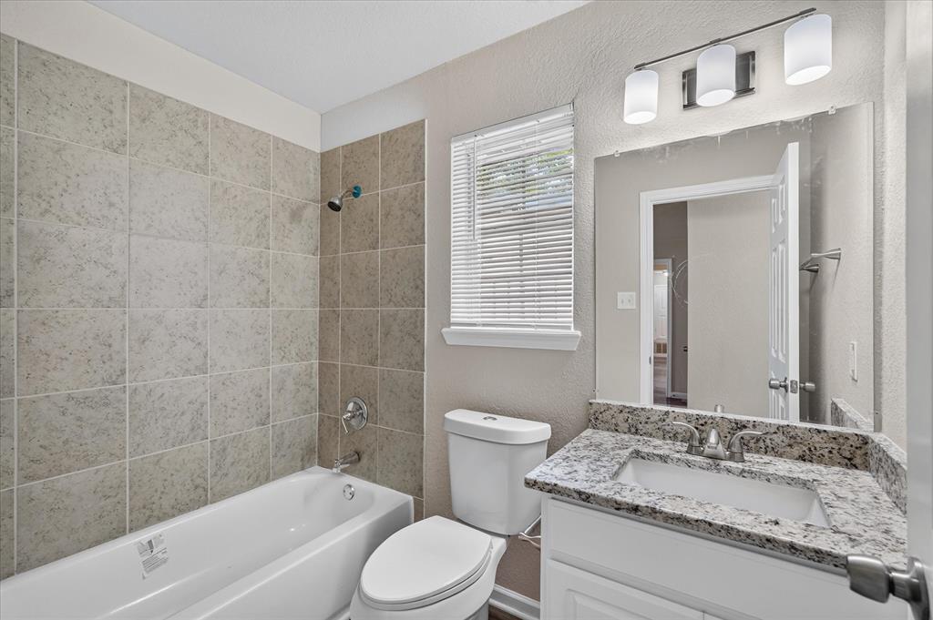 Bathroom featuring a tiled shower surround, white bathtub, vanity with a stone countertop, and an overhead light fixture