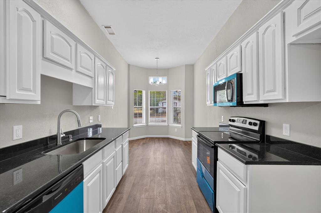 Kitchen featuring white cabinetry, dark countertops, stainless steel sink, wood-finish flooring, and bay windows