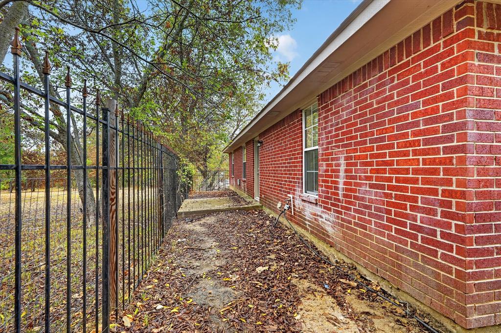 Red brick exterior with white trim, featuring a single window and an ornamental black metal fence