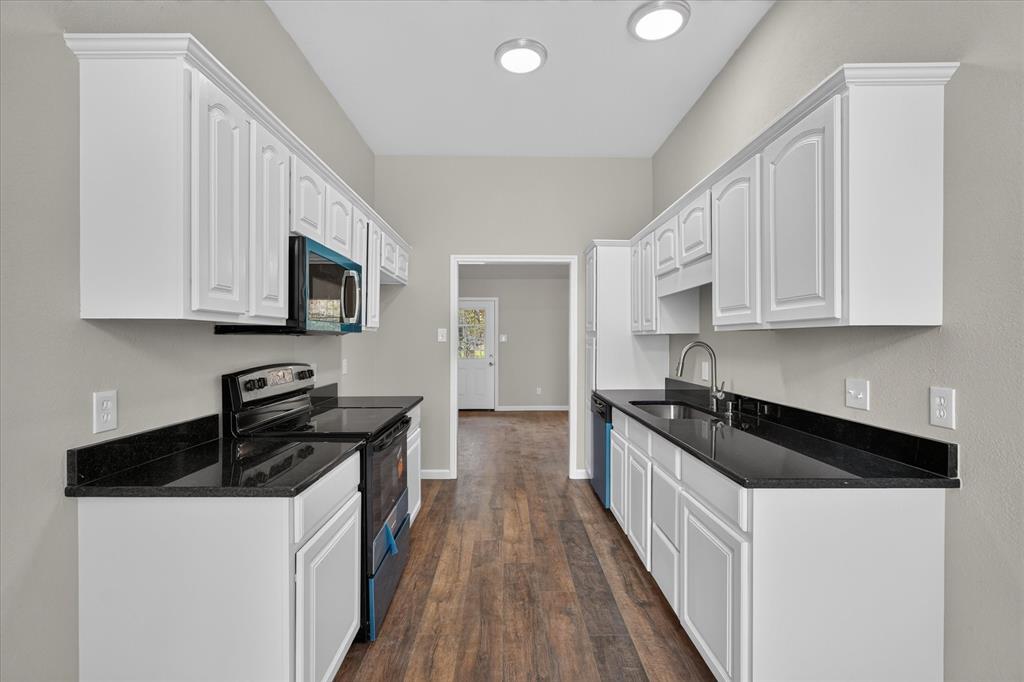White cabinetry with crown molding, black countertops, stainless steel sink with gooseneck faucet, microwave, and wood-finish flooring
