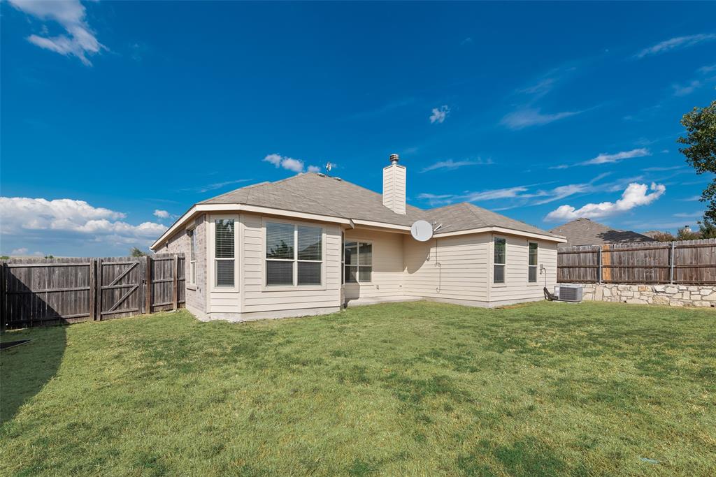 Expansive backyard featuring a wood privacy fence, stone retaining wall, and a multi-pane bay window