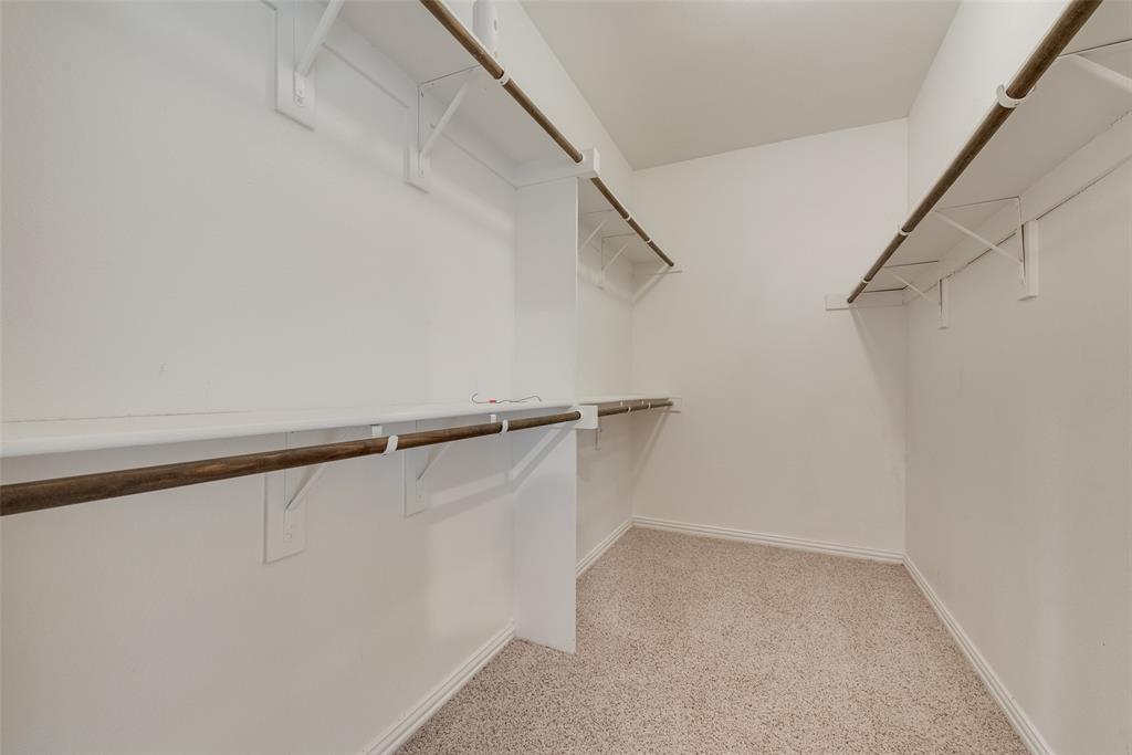 Carpeted walk-in closet featuring white walls, white shelving, and wood-finish hanging rods