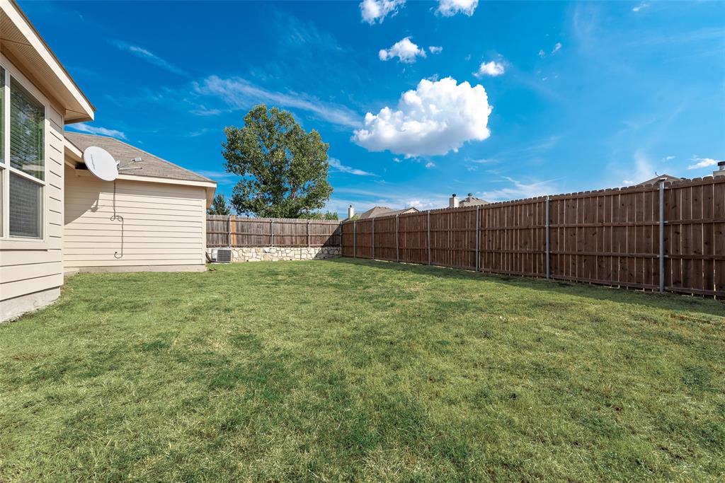 Expansive grassy yard with a privacy fence and stone retaining wall