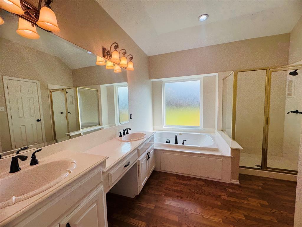 Dual vanity with integrated sinks, built-in soaking tub, separate shower enclosure, and wood-finish flooring