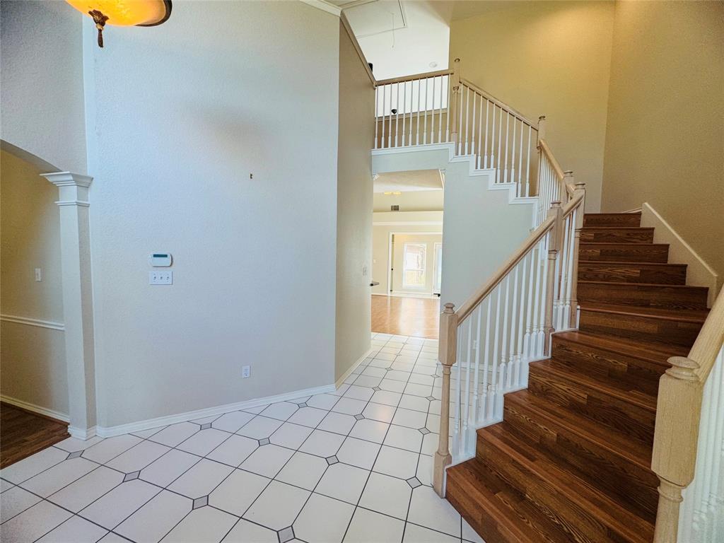 Two-story entryway featuring wood-finish staircase, white balusters, and square tile flooring with decorative inserts Two-story entryway featuring wood-finish staircase, white balusters, and square tile flooring with decorative inserts