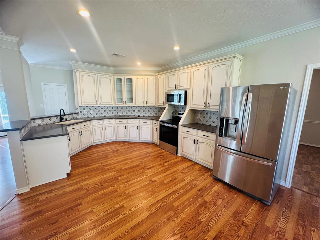 Kitchen featuring wood-finish flooring, recessed lighting, stainless steel appliances, white cabinetry, and a patterned backsplash