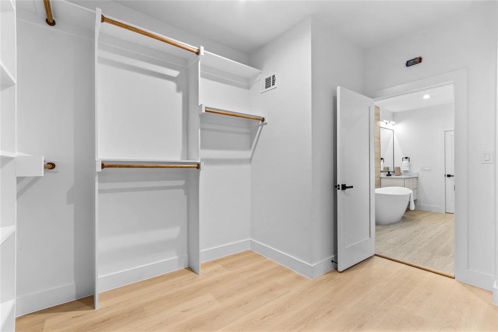 Walk-in closet featuring white built-in shelving, hanging rods, and light wood-finish flooring