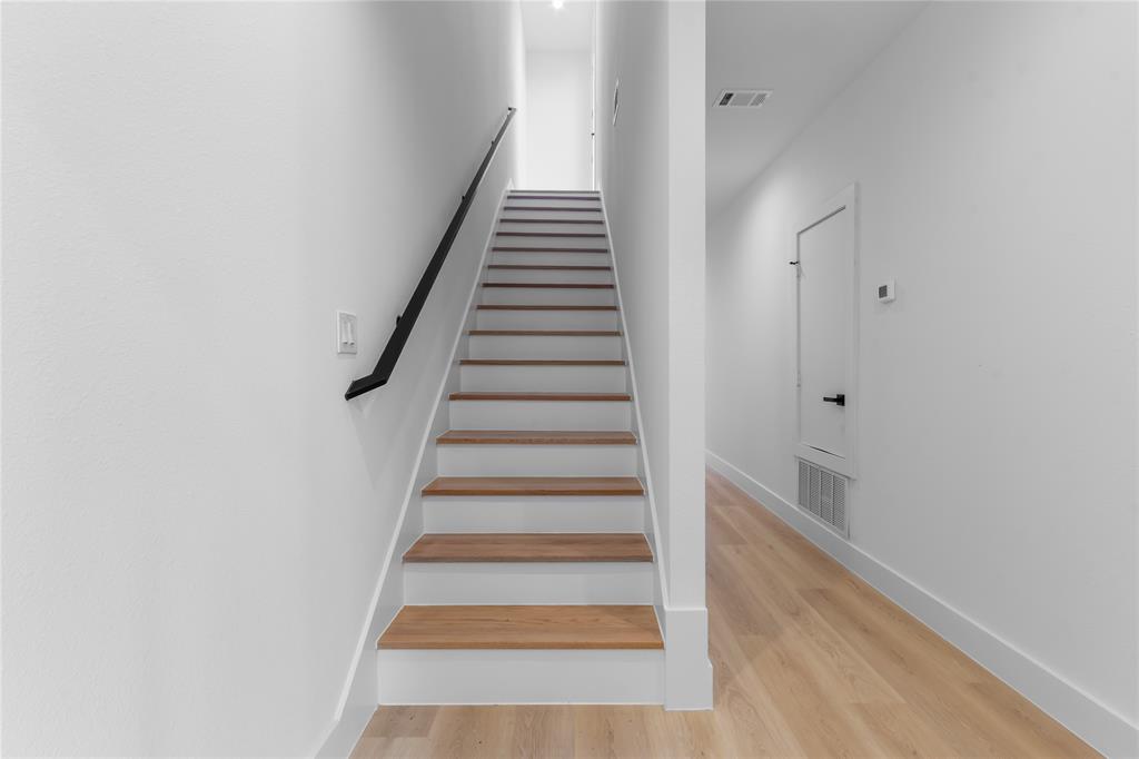 Staircase featuring wood-finish treads and white risers with a black wall-mounted handrail