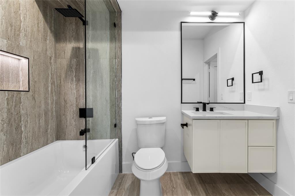 Sleek bathroom featuring a floating vanity with a stone countertop, a rectangular mirror with a black frame, and a tub-shower combination with a glass panel and matte black fixtures