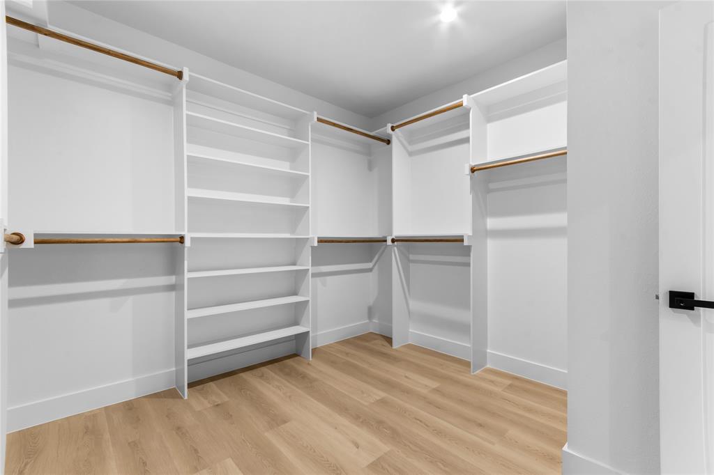 Walk-in closet featuring built-in white shelving, multiple hanging rods, recessed ceiling lighting, and wood-finish flooring